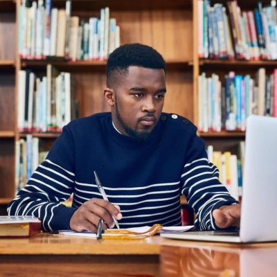 Library, laptop and university student with research, learning and planning for exam, report or focus on computer, studying or education. Black man, college and working on task, essay or scholarship.